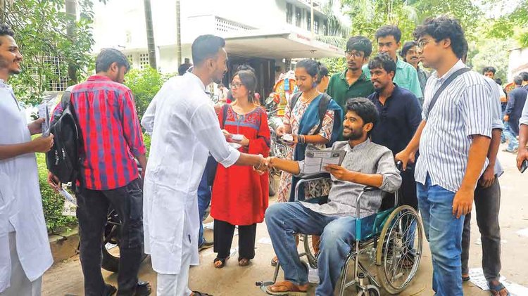 হাসপাতাল থেকে ক্যাম্পাসে এসে হুইলচেয়ারে বসেই ভোটের প্রচারণা চালাচ্ছেন জিএস প্রার্থী মেঘমল্লার বসু। গতকাল মধুর ক্যানটিনের সামনে। ছবি: আজকের পত্রিকা