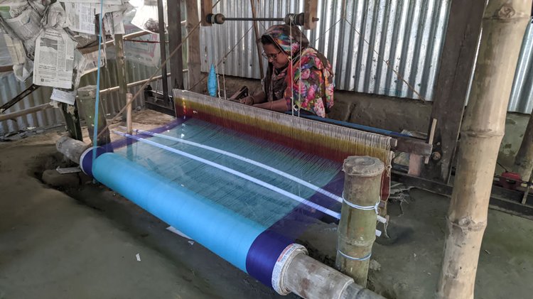 বাড়িতে তাঁত মেশিনে শাড়ি বুনছেন এক নারী। ছবি: আজকের পত্রিকা