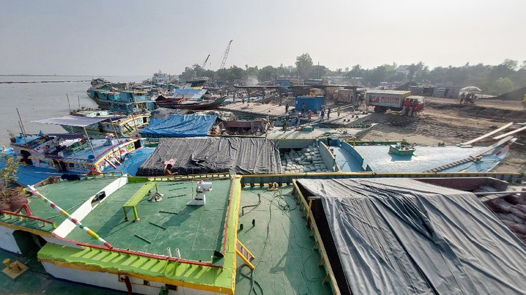 এগিয়ে চলেছে পাবনার নগরবাড়ি নৌবন্দর নির্মাণকাজ। অন্যদিকে চলছে জাহাজ থেকে পণ্য খালাস। রোববার দুপুরে তোলা। ছবি: আজকের পত্রিকা।