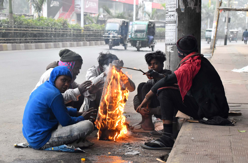 কনকনে ঠান্ডা থেকে বাঁচার জন্য রাস্তার পাশে কয়েকজন আগুন জ্বালিয়ে বসে আছেন। নগরীর রেলস্টেশন মার্কেটের সামনে আজ বুধবার সকাল ৯টার দৃশ্য, রাজশাহী, ১৭ জানুয়ারি ২০২৪। ছবি: মিলন শেখ