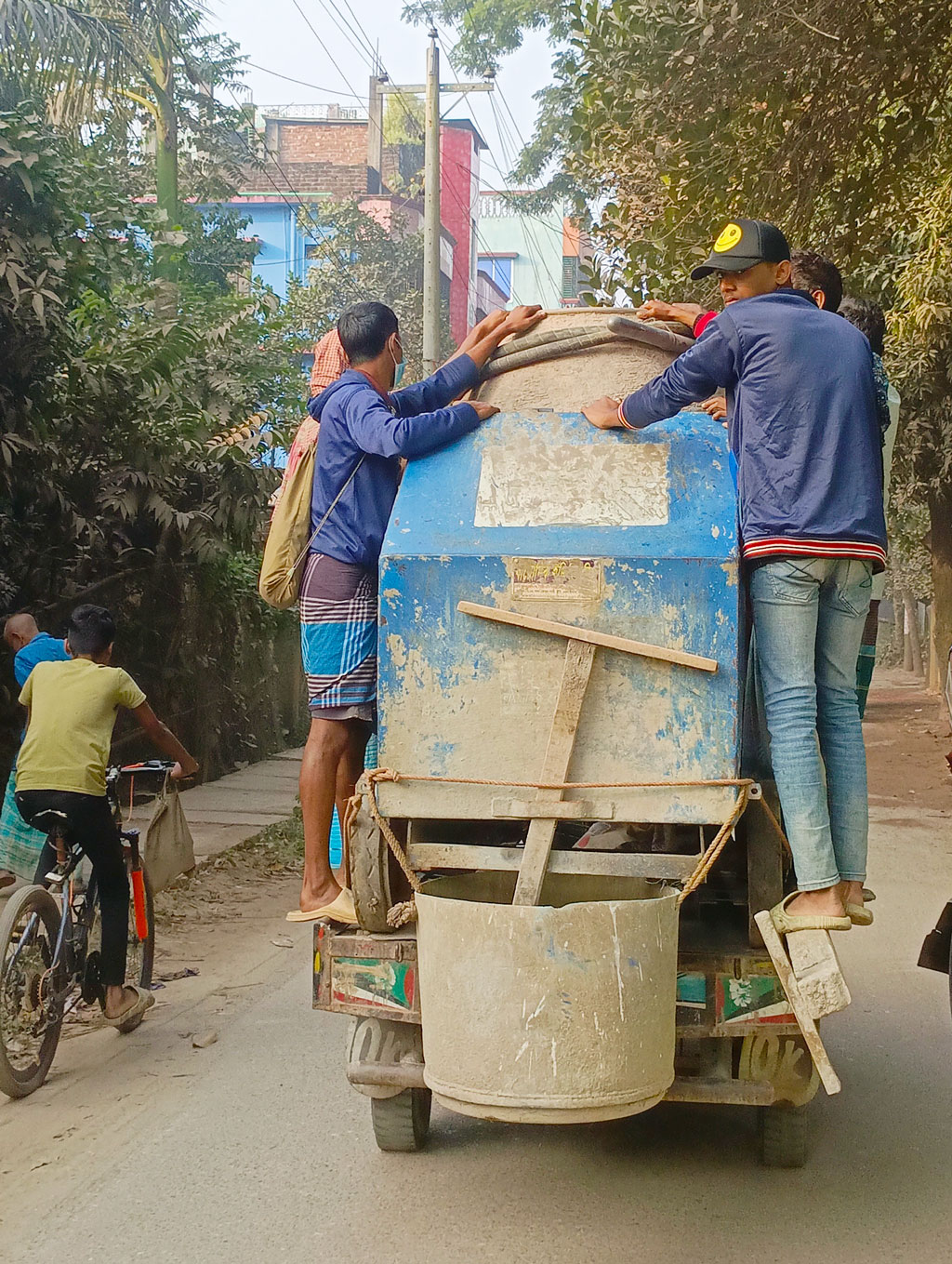 হালকা কুয়াশা শীতের আগমনী সংকেত দিচ্ছে। কিছুটা শীতও পড়তে শুরু করেছে। জীবিকার তাগিদে ঢালাই মেশিনেই ঝুলে ঝুঁকি নিয়ে গন্তব্যে যাচ্ছেন শ্রমিকেরা। রায়পুরার পৌর এলাকার থেকে তোলা, নরসিংদী, ২৬ নভেম্বর ২০২৪। ছবি: হারুনূর রশিদ