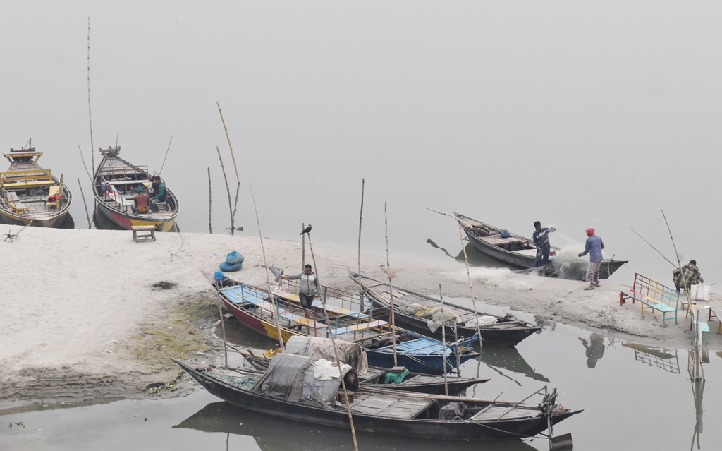 নদীর পাড়ে বেঁধে রাখা ডিঙি নৌকায় জাল ঠিক করছেন জেলে। শ্রীরামপুর টি-বাঁধ, পদ্মার তীর, রাজশাহী। ছবি: মিলন শেখ