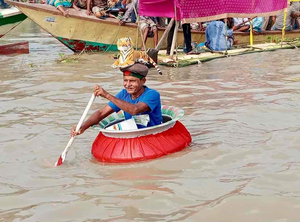 মাথায় জাতীয় পতাকা আর পিঠে বাঘের প্রতিকৃতি এঁকে ডেগচিতে ভর করে কালীগঙ্গা নদীর পানিতে ভেসে নৌকাবাইচ উপভোগ করছেন এক ব্যতিক্রমী দর্শক। এমন অভিনব উৎসাহ ও উদ্দীপনার স্বীকৃতি হিসেবে আয়োজক কমিটি তাঁকে ‘সেরা দর্শক’ সম্মাননায় ভূষিত করে। শনিবার মানিকগঞ্জের বেউথা এলাকা থেকে তোলা। ছবি: আব্দুর রাজ্জাক