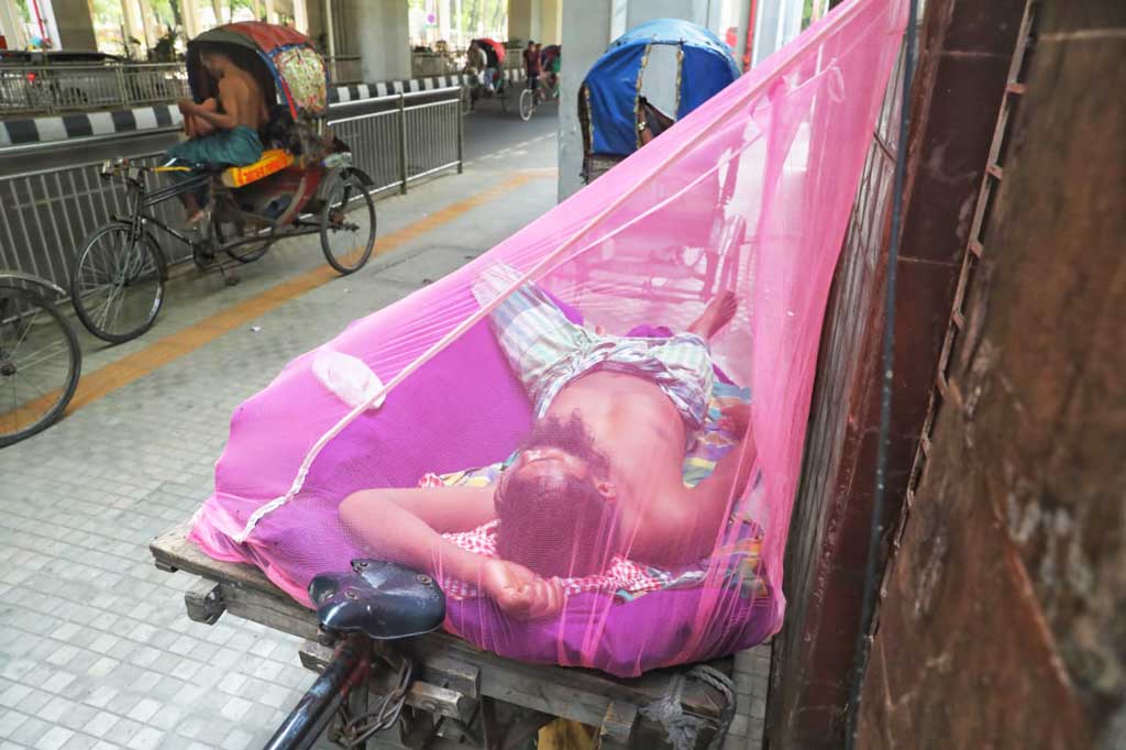 একদিকে প্রচণ্ড গরম অন্যদিকে মশার উপদ্রব বেড়েই চলছে। মশার হাত থেকে বাঁচতে দিনের বেলায় মশারি টাঙিয়ে রাস্তার পাশে শুয়ে আছে শ্রমজীবী দিনমজুর। টিএসসি মেট্রো রেলস্টেশন, ঢাকা, ২৫ এপ্রিল ২০২৪।ছবি জাহিদুল ইসলাম।