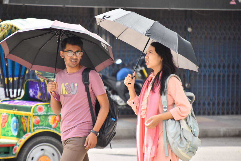 তপ্ত দুপুরে হাপিত্যেশ মানুষের। তবুও প্রয়োজনে ঘর থেকে বের হতে হচ্ছে। প্রখর রোদ থেকে বাঁচতে ছাতা মাথায় হেঁটে যাচ্ছেন তরুণ-তরুণী। নগরী লক্ষীপুর এলাকা, রাজশাহী, ২১ এপ্রিল, ২০২৪। ছবি: মিলন শেখ