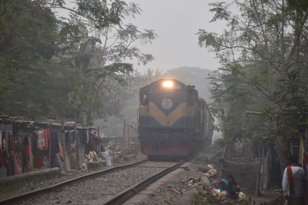 কুয়াশায় ঢাকা সকাল। সূর্যের দেখা নেই। ঘন কুয়াশার কারণে হেডলাইট জ্বালিয়ে চলাচল করছে ট্রেন। শীত থেকে বাঁচতে রেললাইনের ধারে আগুন জ্বালিয়ে বসে আছে সাধারণ মানুষ। ছবিটি রাজশাহী নগরীর নামো ভদ্রা রেললাইন এলাকা থেকে আজ সকাল ১০টায় তোলা। ছবি: মিলন শেখ