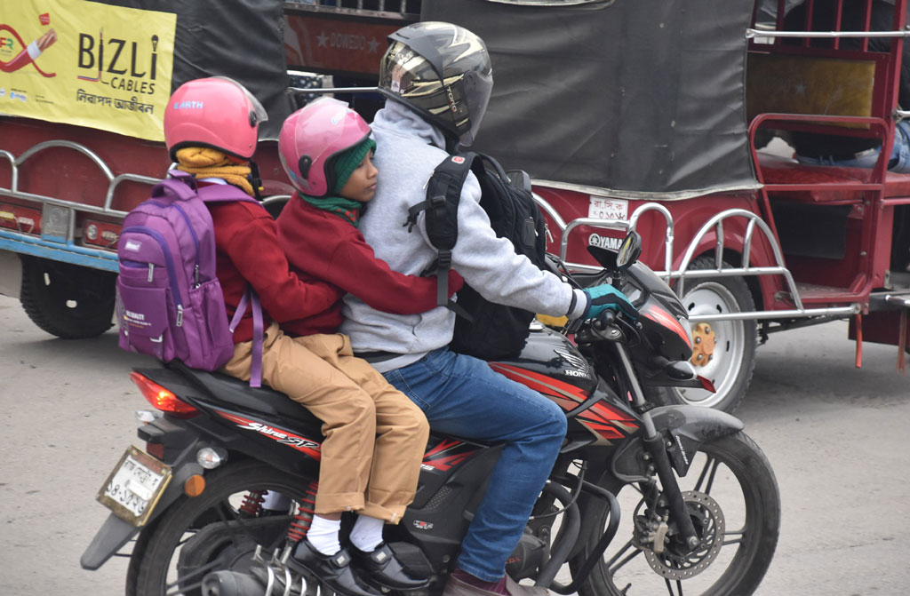 দুই শিশুসন্তানকে মোটরসাইকেলের পেছনে বসিয়ে শীতের সকালে বিদ্যালয়ে নিয়ে যাচ্ছেন বাবা। শিশু দুটি জবুথবু হয়ে তাদের বাবাকে আঁকড়ে ধরে বসে আছে। রাজশাহী নগরীর রেলগেট এলাকা থেকে আজ সকালে তোলা। ছবি: মিলন শেখ