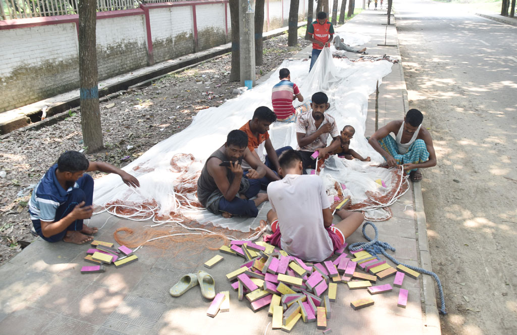 পদ্মা নদীর পানি কখনো বাড়ছে আবার কখনো কমছে—এই ওঠানামার মধ্যেই ব্যস্ত সময় কাটাচ্ছেন স্থানীয় জেলেরা। নদীর তীরঘেঁষা রাস্তায় গাছের ছায়ায় বসে তাঁরা নতুন জাল তৈরির কাজে মগ্ন। আজ সকালে শ্রীরামপুর এলাকা থেকে তোলা। ছবি: মিলন শেখ