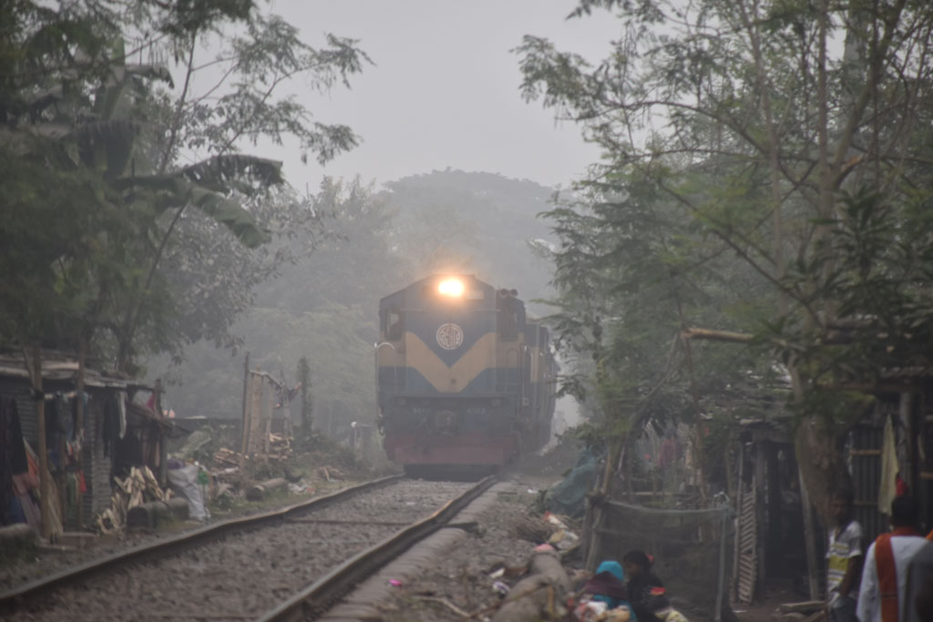 কুয়াশায় ঢাকা সকাল। সূর্যের দেখা নেই। ঘন কুয়াশার কারণে হেডলাইট জ্বালিয়ে চলাচল করছে ট্রেন। শীত থেকে বাঁচতে রেললাইনের ধারে আগুন জ্বালিয়ে বসে আছে সাধারণ মানুষ। ছবিটি রাজশাহী নগরীর নামো ভদ্রা রেললাইন এলাকা থেকে আজ সকাল ১০টায় তোলা। ছবি: মিলন শেখ