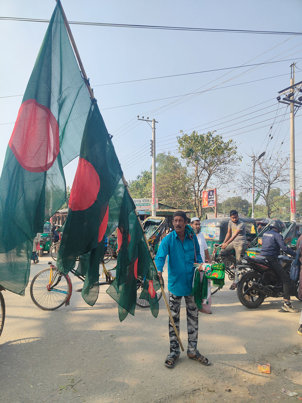 শহীদ বুদ্ধিজীবী দিবস ও মহান বিজয় দিবস উপলক্ষে জাতীয় পতাকা বিক্রি বেড়েছে। তবে অন্যান্য বছরের তুলনায় এবার বেচাকেনা কম বলে জানিয়েছেন মাদারীপুর জেলার চাঁনমিয়া নামের এই পতাকা বিক্রেতা। সিরাজগঞ্জ সদরের বাজার স্টেশন এলাকা থেকে আজ দুপুরে তোলা। ছবি: আব্দুল্লাহ আল মারুফ