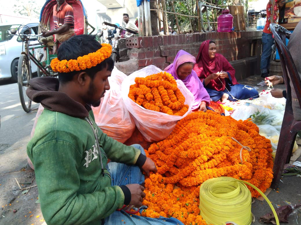 পয়লা ফাল্গুনকে কেন্দ্র করে হলুদ গাঁদার মালা তৈরি করছেন এক দোকানি। 