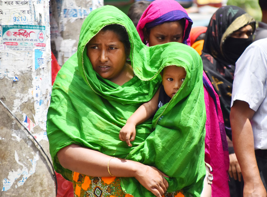 তীব্র দাবদাহে নাকাল জনজীবন। অতি প্রয়োজন ছাড়া ঘর থেকে বের হচ্ছেন না মানুষ। জীবিকার তাগিদে গরম উপেক্ষা করে শিশুকে কোলে নিয়ে বের হয়েছেন এ নারী। গরম তাপ থেকে কিছুটা রক্ষা পেতে নিজের গায়ে থাকা ওড়না দিয়ে শিশুকে ঢেকে রেখেছেন। নগরী লক্ষীপুর এলাকা, রাজশাহী, ২১ এপ্রিল, ২০২৪। ছবি: মিলন শেখ