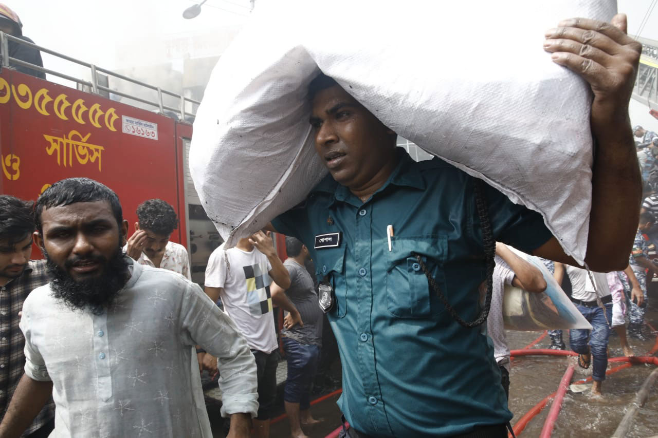 মাথায় নিয়ে ব্যবসায়ীদের মালামাল নিরাপদ স্থানে সরিয়ে নিচ্ছেন এক পুলিশ সদস্য
