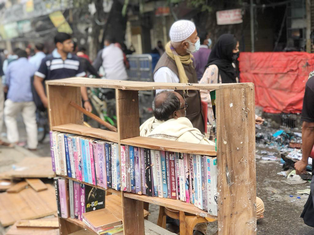 মনের দুঃখে দোকানের সামনে বসে দেখছেন পুড়ে যাওয়া বইয়ের দোকান