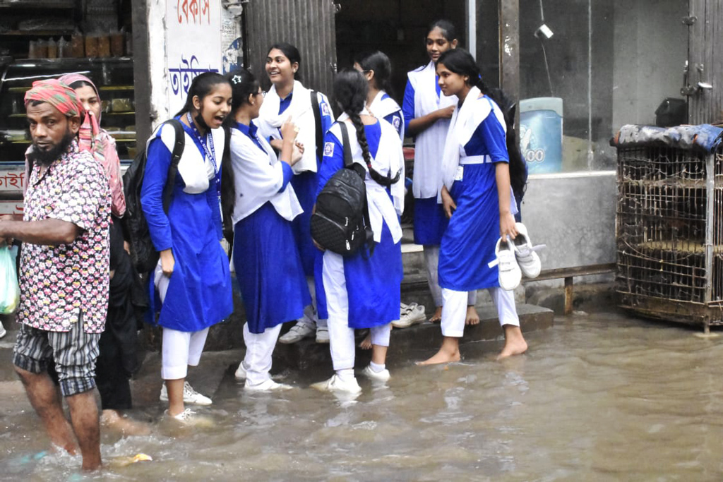 গলিতে জমে থাকা বৃষ্টির পানি বাড়িয়েছে দুর্ভোগ। পথের মাঝে জলাবদ্ধতার পানি থেকে রক্ষায় কয়েক ছাত্রী দাঁড়িয়ে আছে সিঁড়িতে কেউবা পায়ের কেডস হাতে ধরে আছে। কদমতলী একে স্কুল এন্ড কলেজের সামনে। ছবি: মেহেদী হাসান