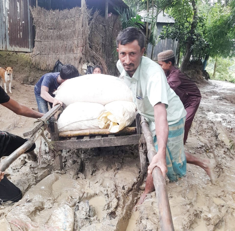 কাদামাটিতে আটকে গেছে ঠেলাগাড়ি। কয়েকজন মিলে ঠেলে পাড় করছেন গাড়িটি। ছবি: আজকের পত্রিকা