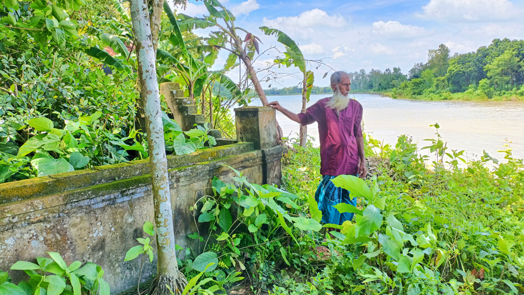 ভাঙনকবলিত স্থানে মায়ের কবরের পাশে দাঁড়িয়ে আছেন দানশীল সমাজসেবক ছোরহাব উদ্দিন। ছবি: আজকের পত্রিকা